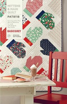 a table with a red chair next to a quilt on the wall and a book