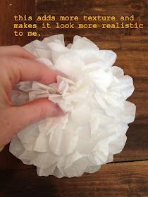 a hand holding a white flower on top of a wooden table next to a piece of paper