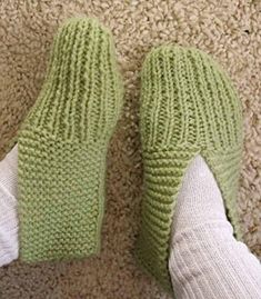 someone's feet wearing green knitted slippers on carpeted area with white leggings