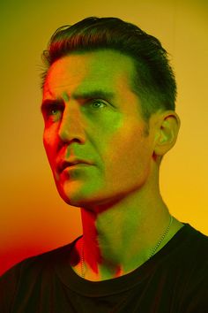 a man with green and red paint on his face looking off to the side while wearing a black t - shirt