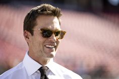 a close up of a person wearing sunglasses and a tie with a baseball field in the background