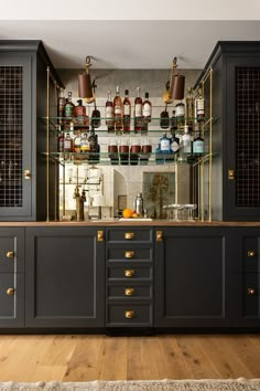 a kitchen with lots of bottles on the wall and shelves above it, along with wooden flooring