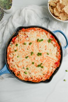 a skillet filled with cheese and veggies next to chips