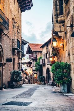 an alleyway with stone buildings and potted plants on either side, in the evening