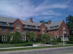 a large brick building with many windows and bushes in front of it on a cloudy day