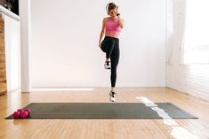 a woman in pink top and black leggings standing on yoga mat talking on cell phone