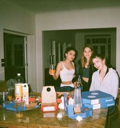 three girls standing around a table with drinks and boxes on it, all smiling for the camera