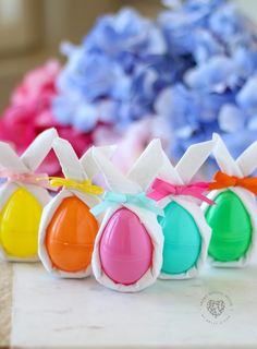 colorful candy eggs with bows on them sitting on a table next to blue and pink flowers