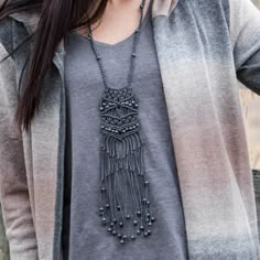 a woman wearing a gray shirt with a black tasseled necklace on her neck