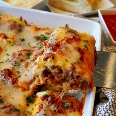 a white plate topped with lasagna covered in cheese and sauce next to bread