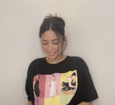 a woman is smiling while using her cell phone in front of a white wall and wearing a t - shirt with an image on it