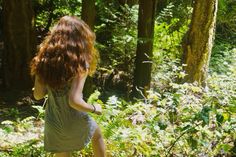 a woman walking through the woods with her hair blowing in the wind on a sunny day