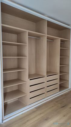 an empty walk in closet with wooden shelves and drawers on the wall, next to a hardwood floor