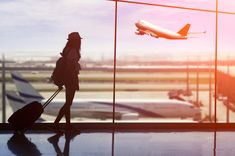 a woman is standing in front of an airport window with her luggage and looking out at the planes