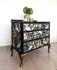 an ornate chest of drawers with birds painted on the front and sides, along with a potted plant