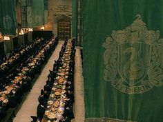 a large dining hall filled with tables and people sitting at long tables in front of a green banner