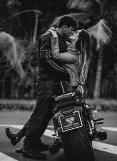 a man and woman kissing on the back of a motorbike with palm trees in the background