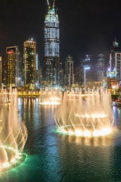 the fountains are lit up at night with city lights in the background