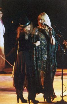 two women standing next to each other on stage with microphones in their hands and one wearing a hat