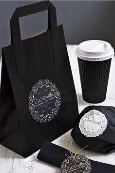 black paper bags with white doily on them next to a coffee cup and bag