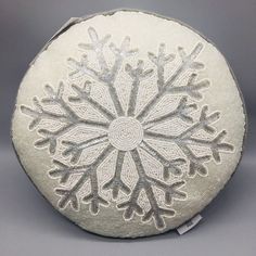 a white round pillow with snowflakes on the front and sides, sitting on a gray surface