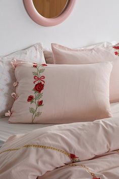 a bed with pink sheets and pillows in front of a round mirror on the wall