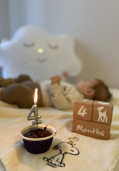 a baby laying in bed next to a birthday candle