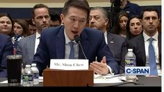 a man in a suit and tie sitting at a table with other people behind him