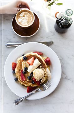 pancakes with fruit and ice cream on a plate next to a cup of cappuccino