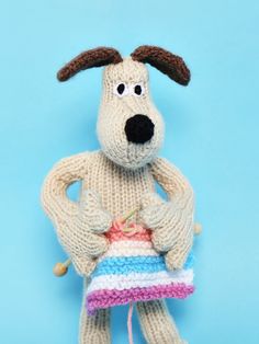 a knitted dog holding a colorful object on a blue background in the shape of a sweater