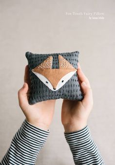 a person holding up a small pillow with a fox design on it's face