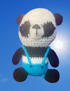 a crocheted panda bear hanging in the air on a sunny day with blue skies