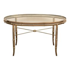 a round glass table with metal legs and a gold frame around the top, against a white background