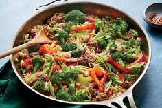 a skillet filled with meat and vegetables on top of a blue table cloth next to a wooden spoon