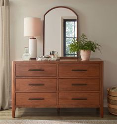 a dresser with a mirror, lamp and potted plant