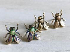 three tiny figurines of different colors and sizes on a white surface, with one wearing a green striped shirt