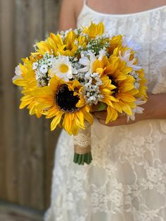 a bride holding a bouquet of sunflowers and daisies