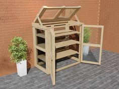 a small wooden structure sitting on top of a brick floor next to a potted plant