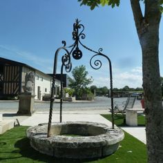 an iron sculpture in front of a building with a tree on the lawn and benches around it