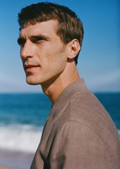 a man standing in front of the ocean with his eyes closed and looking off into the distance