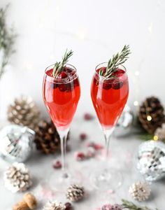 two glasses filled with red wine and garnished with rosemary sprigs, surrounded by christmas decorations