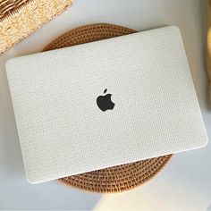 an apple laptop sitting on top of a table next to a straw hat and wicker basket