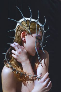 a woman with metal spikes on her head and hands wrapped around her neck, posing for the camera