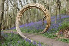 a wooden arch in the middle of a forest with bluebells growing around it