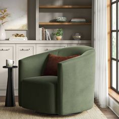 a green chair sitting in front of a window next to a table with a vase on it