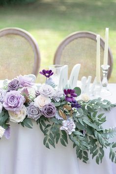 the table is set with purple and white flowers, greenery, candles and napkins