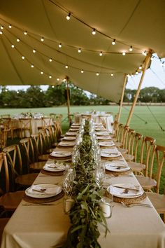 a long table set up with place settings for dinner in the middle of a field