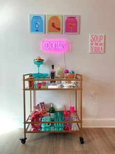 a bar cart with drinks on it in front of a neon sign that reads cocktails