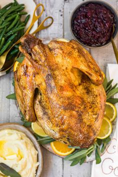 a roasted turkey on a platter with lemons, green beans and cranberry sauce