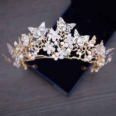 a gold tiara with white flowers and butterflies on the headpiece is sitting on a black velvet box